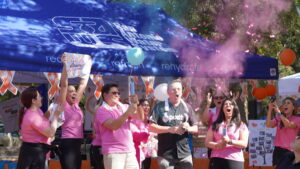 A group of people from Pozitivf Fertility wearing pink shirts and one person in a black shirt with a Pozitivf Fertility towel around his neck are gathered at an outdoor park. Some people are holding balloons, and pink confetti is being thrown into the air. Orange and white ribbons decorate the area. This image captures Pozitivf's spirit of community and celebration at the Walk of Hope 2024.